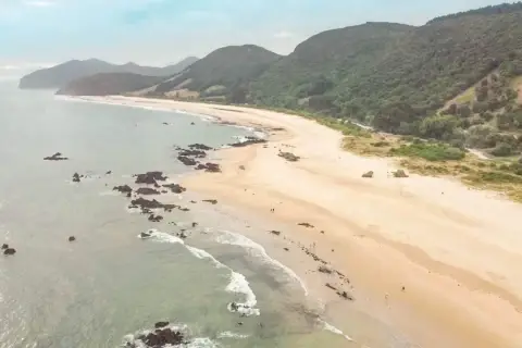 Vista aérea de la **playa Trengandin**, con arena dorada, rocas oscuras y colinas verdes al fondo.