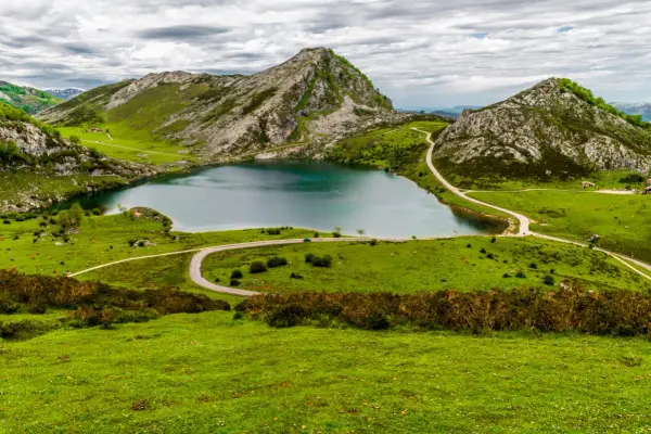 Lago en Picos de Europa que ver: paisaje verde con montañas rocosas, un lago azul y carreteras sinuosas.